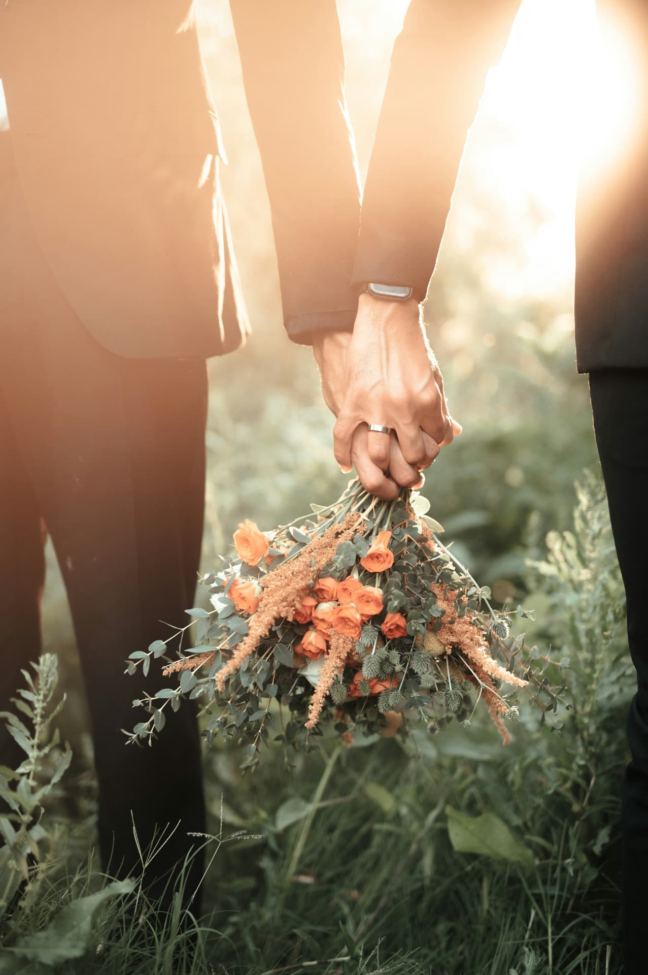 Dos personas tomadas de la mano con un ramo de rosas naranjas