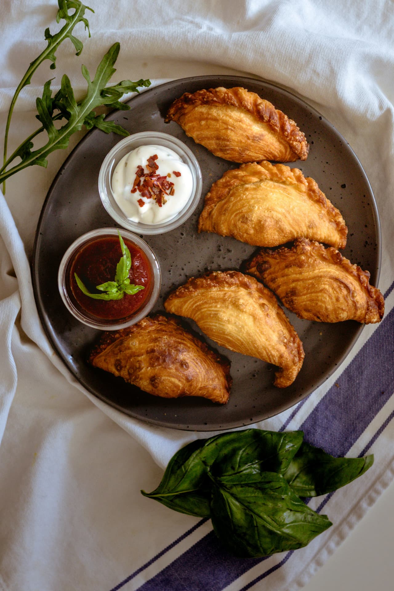 Empanadas doradas servidas con salsas y hierbas frescas